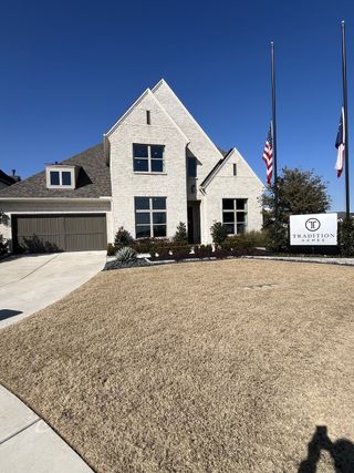 Street view A beautiful white brick home with sharp gables and manicured landscaping in The Parks at Wilson Creek by Tradition Homes (Celina, TX).