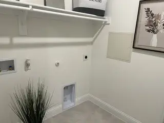 A functional laundry room with a shelf, modern connections, framed art, and tile flooring.
