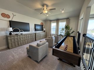 Model Home A cozy entertainment room with dual TVs, plush seating, and a shuffleboard table, featuring stylish decor and a bright window view.