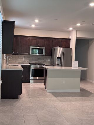 A modern kitchen with dark cabinetry, stainless steel appliances, sleek countertops, and ample natural light.