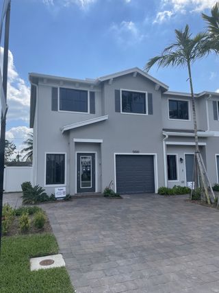 Modern gray home with palm trees and a paved driveway in Ashwood Cove by D.R. Horton (Lake Worth, FL).