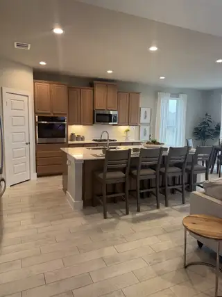 Model Home A modern kitchen with wooden cabinets, an island with bar seating, and sleek appliances, creating a warm, inviting space.