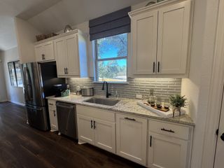A modern kitchen with sleek white cabinets, granite countertops, stainless steel appliances, and elegant backsplash tiles.