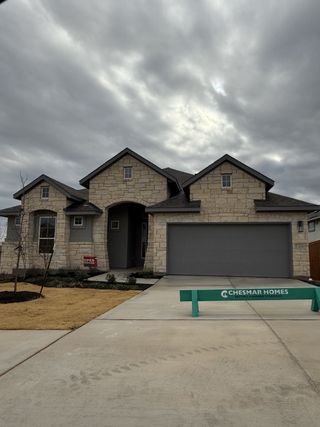 Street view A charming stone facade home with a spacious garage in Lariat by Chesmar Homes (Liberty Hill, TX).