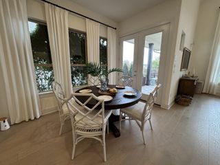 Model Home A cozy dining area with a round table, elegant white chairs, and floor-to-ceiling windows opening to a serene patio.