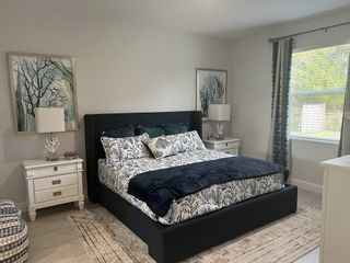 A serene bedroom featuring a dark upholstered bed, botanical prints, and soft natural light filtering through a window.