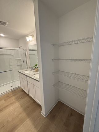 A sleek bathroom with granite countertops, a white vanity, and wood flooring in Blue Ridge Ranch by Rosehaven Homes (San Antonio, TX).