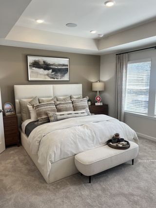 A sophisticated primary suite featuring a plush bed, neutral tones, and a cozy seating bench.