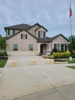 Model Home Elegant white brick home with dark shutters and lush landscaping in Kings Way by M/I Homes (Denton, TX).