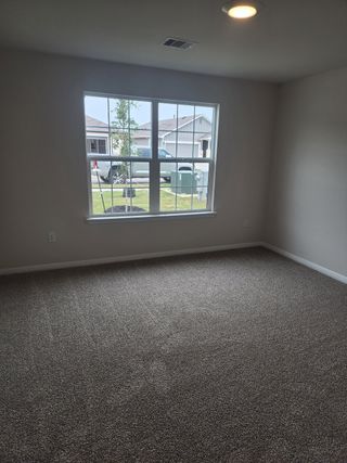 Model Home A bright room with plush carpeting and a large window letting in natural light.