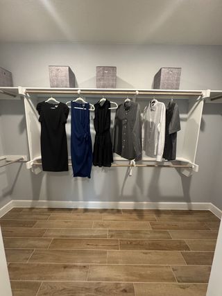 Model Home A spacious walk-in closet with wooden flooring, organized clothing, and storage bins.