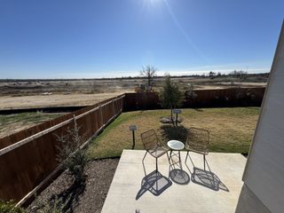 Model Home A backyard patio with seating, overlooking a fenced yard and open field.