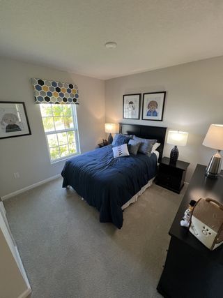 Cozy bedroom with soft carpet, dark wood furniture, playful wall art, and a navy bedspread. Brightened by natural light.