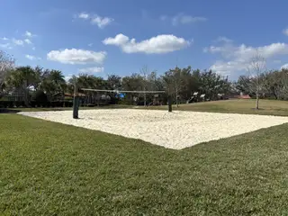 Community Amenities A sand volleyball court surrounded by lush greenery, offering outdoor recreation in Kindred by D.R. Horton (Kissimmee, FL).