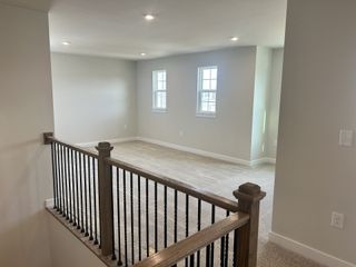 A bright, open loft with soft carpeting, neutral walls, and recessed lighting, complemented by a modern wooden railing.