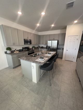 Model Home A gourmet kitchen with gray shaker cabinets, granite countertops, stainless steel appliances, and an island with bar seating.