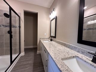 A modern bathroom featuring a dual-sink granite vanity, sleek mirrors, and a spacious glass-enclosed shower.