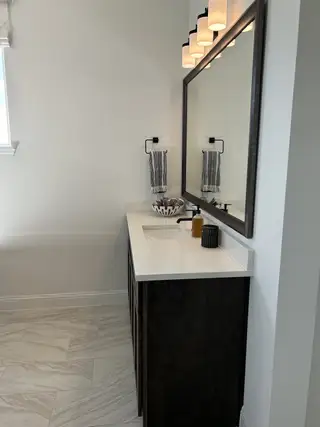A sleek bathroom with a dark wood vanity, large mirror, and elegant lighting.