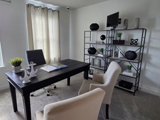 Modern home office with a sleek black desk, elegant white chairs, and stylish shelving for a chic and functional workspace.