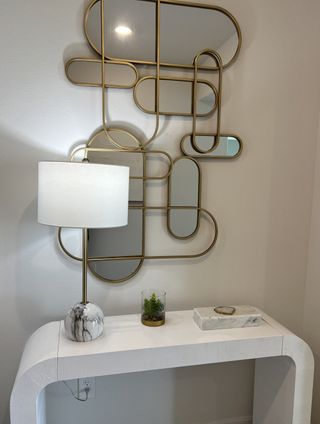 Model Home A chic entryway with a modern geometric mirror, marble lamp, and sleek white console table with decorative accents.
