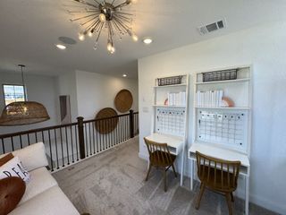 A bright loft space with dual workstations, open shelving, a modern chandelier, and a view overlooking the lower level.