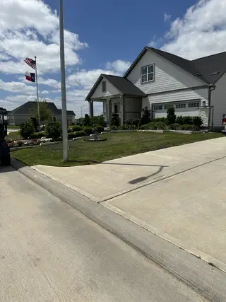 Street view A charming home with manicured landscaping in Winfrey Estates by ROC Homes (Tomball, TX), featuring two flags and a sunny sky.