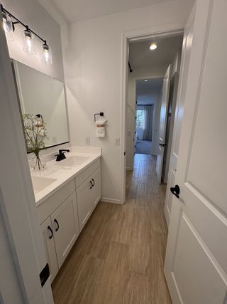 A sleek bathroom featuring a double vanity, modern lighting, and light wood flooring.