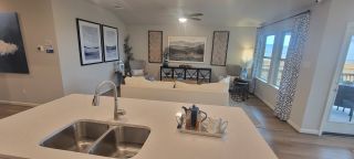 A bright, open-concept living space in a Remington Ranch home, featuring a modern kitchen island, living room with neutral decor, and large windows (San Antonio, TX).