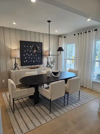 Model Home A chic dining area with a sleek black table, modern lighting, beige chairs, and elegant wall art on light wood floors.
