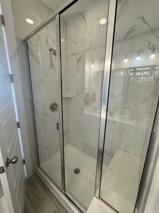 A sleek shower with marble-patterned tiles and a glass door, creating a modern and elegant bathroom design.