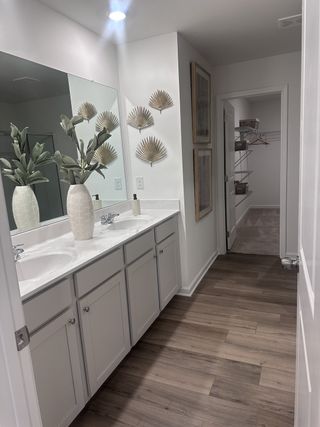 A modern bathroom featuring dual sinks, elegant decor, and sleek wooden floors, leading to a spacious closet.