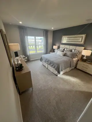 Model Home A cozy bedroom featuring a plush bed, soft lighting, and elegant decor with a large window inviting natural light.