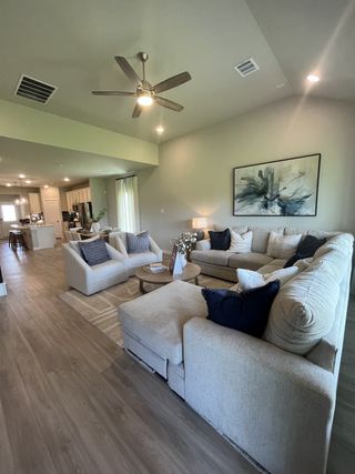 Spacious living area with a large sectional, modern ceiling fan, and artful decor on wood flooring.
