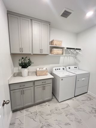A sleek laundry room with gray cabinetry, marble-tiled floors, and a spacious countertop for folding and organization.