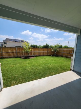 A covered patio leading to a lush, fenced backyard with clear blue skies above.