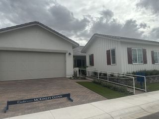 A charming white home with contrasting maroon shutters and a paved driveway leading to an attached garage in McKinley Glenn by Cachet Homes Arizona (Chandler, AZ).