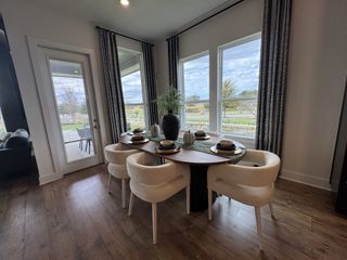 Model Home A chic dining area with a wooden table, elegant white chairs, large windows, and a view of the patio and outdoors.