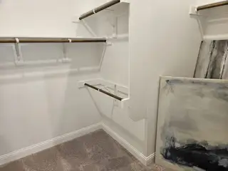 A spacious walk-in closet with wooden rods, plush carpet, and abstract artwork leaning against the wall.