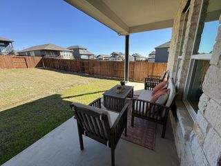 A cozy covered patio with outdoor seating overlooks a spacious fenced yard, perfect for relaxation and enjoyment.