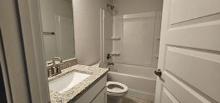 A modern bathroom with a granite countertop, sleek faucet, and a combination tub-shower unit.