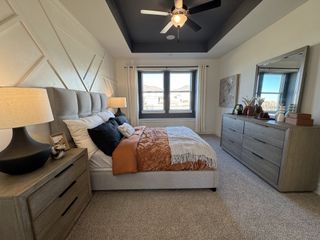 A cozy bedroom featuring a textured accent wall, plush bedding, and modern furniture with natural light streaming through large windows.