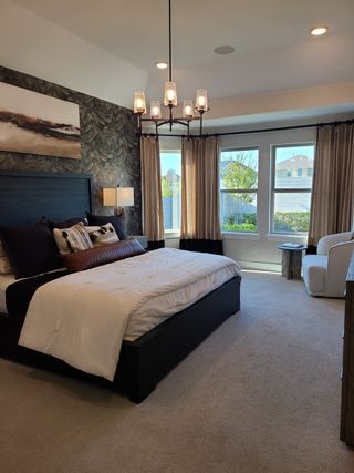 A cozy bedroom with a textured accent wall, elegant chandelier, and large windows for natural light.