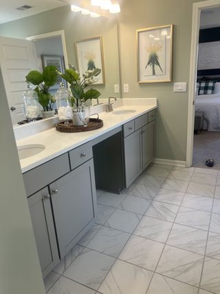 Elegant bathroom with dual sinks, marble-tiled floor, and tasteful decor featuring green accents and modern lighting.
