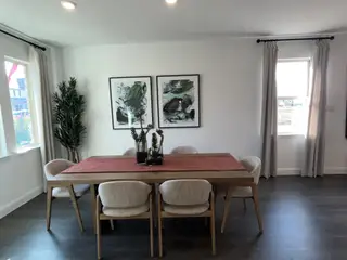 A modern dining room with abstract art, elegant curtains, and a wooden table set for six on dark hardwood floors.