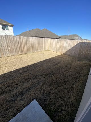 A compact backyard enclosed by a wooden fence, featuring a concrete patio and dry grass.