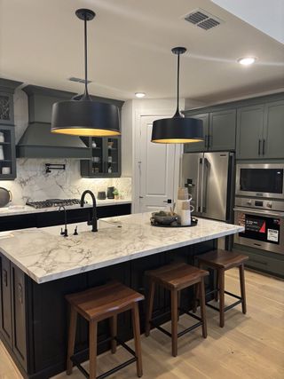 A chic kitchen with a marble island, sleek black lighting, and modern stainless steel appliances.