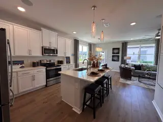 A chic kitchen and living area featuring white cabinetry, wood floors, a central island, and modern decor.