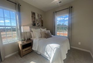 A bright bedroom with a cozy white bed, large windows, and elegant artwork, offering natural light and a serene atmosphere.