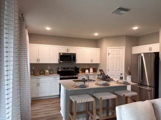Modern kitchen with sleek white cabinets, stainless steel appliances, and a cozy breakfast bar with striped stools.