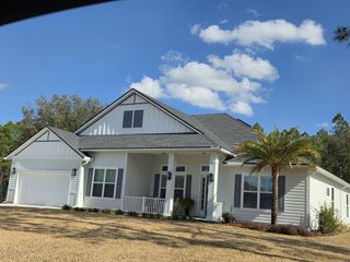 Street view A charming white home with a gabled roof and lush landscaping in Edwards Creek Estates by SEDA New Homes (Jacksonville, FL).